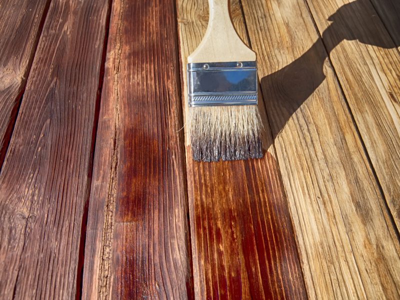 a wooden brush covers the wooden plank surface with a dark red stain front side view close up
